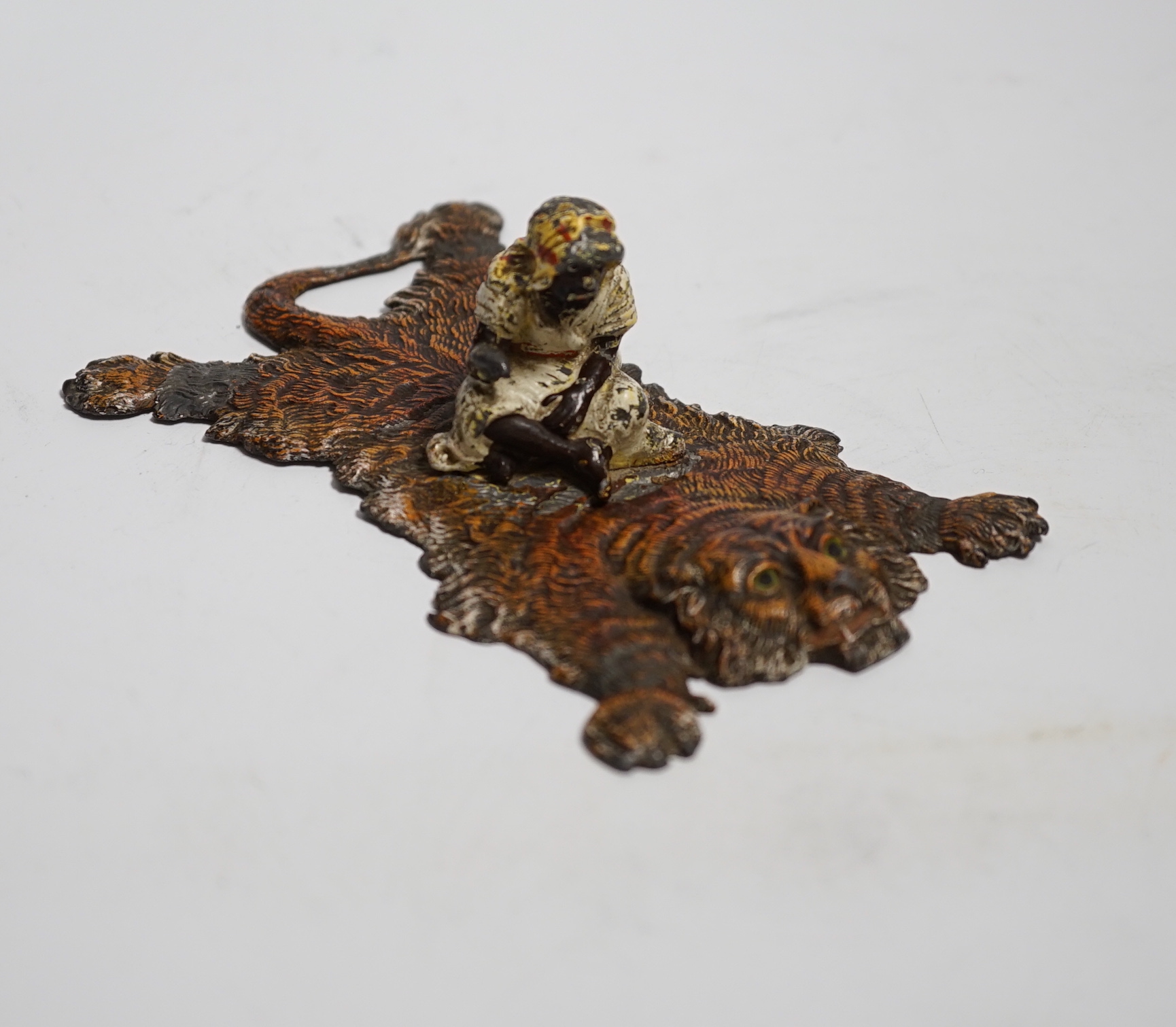 A Bergmann style painted lead figure of a gentleman on a tiger skin, 12.5cm long